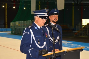 Przemówienie przy mównicy Komendanta Powiatowego Policji w Tomaszowie Mazowieckim. W tle widoczny lektor uroczystości.