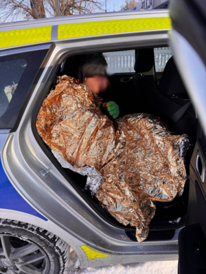 Wyziębiony mężczyzna okryty kocem termicznym siedzący w radiowozie oznakowanym.