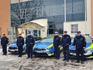 Komendant Powiatowy Policji w Tomaszowie Maz. insp. Tomasz Jędrzejczyk wraz z kadrą kierowniczą na tle budynku KPP w Tomaszowie Maz. oraz nowych oznakowanych radiowozów.