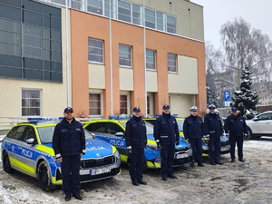 Komendant Powiatowy Policji w Tomaszowie Maz. insp. Tomasz Jędrzejczyk wraz z kadrą kierowniczą na tle budynku KPP w Tomaszowie Maz. oraz nowych oznakowanych radiowozów.