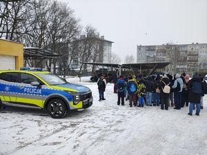 Dzieci z półkolonii odwiedzające komendę w trakcie oglądania policyjnych radiowozów.