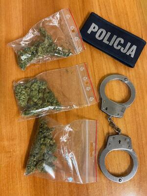 Zabezpieczone narkotyki na tle policyjnych kajdanek i opaski z napisem Policja.