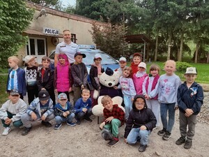 Dzieci i umundurowany Policjant na tle komisariatu konnego.