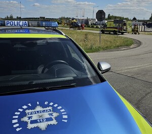 Na pierwszym planie policyjny radiowóz, w tle pojazd karetki pogotowia oraz śmigłowiec