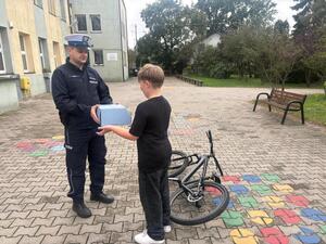 Umundurowany Policjant wręczający kask chłopcu.