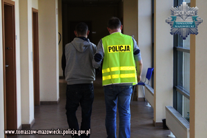 Policjant prowadzi korytarzem zatrzymanego mężczyznę