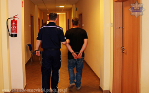 umundurowany policjant prowadzi korytarzem budynku komendy zatrzymanego mężczyznę w sprawie rozboju na starszej kobiecie, który na nadgarstkach ma nałożone kajdanki