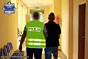 Policjant prowadzi korytarzem zatrzymanego mężczyznę